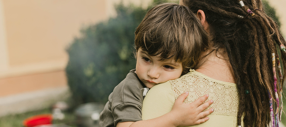 A woman holds a young toddler boy as he wraps his arm around her shoulder