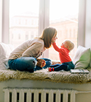 Young child touching mom's face seated next to window