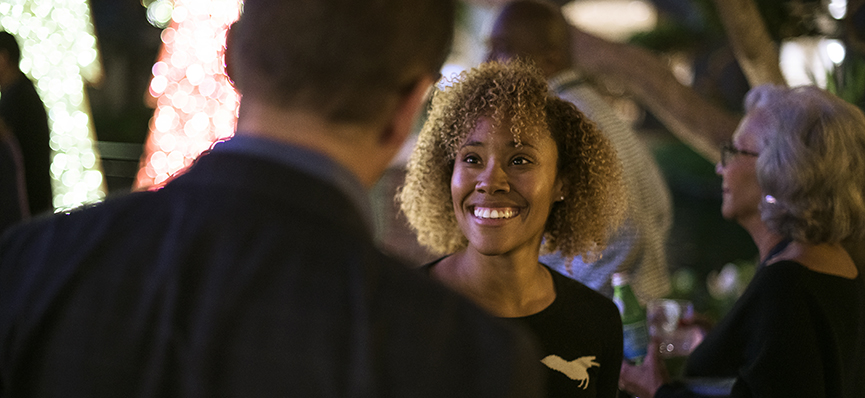 Woman smiling and talking to man with his back facing the camera at an event