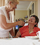 Older female direct support professional standing next to seated woman with a disability